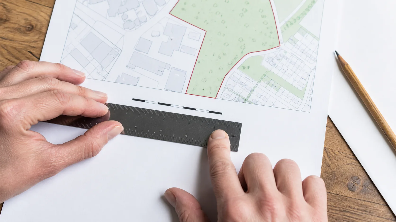 Hands measuring the scale bar on a printed planning map with a ruler