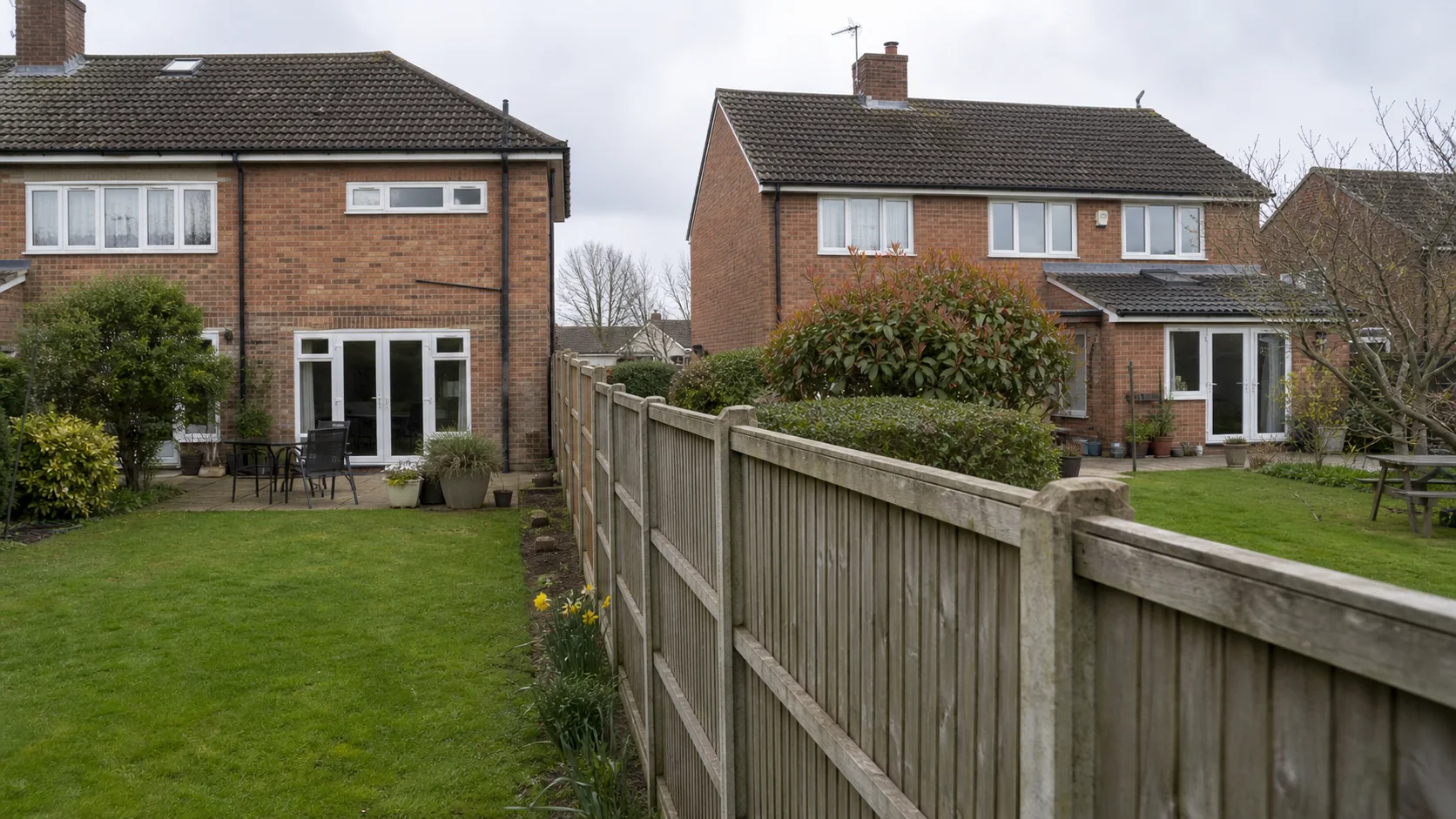 A timber fence running between two ordinary British back gardens